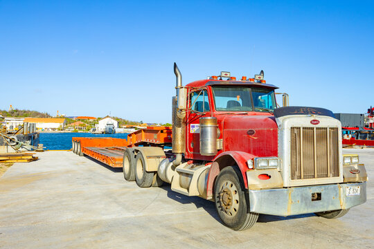 Willemctad, Curacao - 22.03.2026: Red classic Peterbilt semi truck with lowboy trailer parked in a harbor area under a clear blue sky