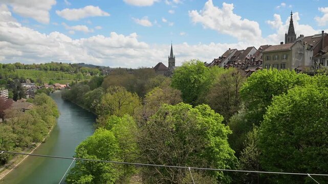 Scenic riverside view with spring trees, rooftops, and church spire under a cloudy blue sky in Morges, Switzerland.