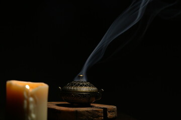 Texture smoke from incense aroma stick in vintage holder box motion rising above in stands near burning candle fire on copy space dark background. Meditation, yoga, wellness relaxation concept © Anastasia.photoyoga