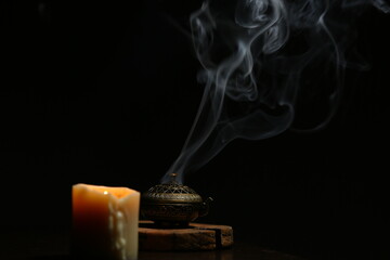 Texture smoke from incense aroma stick in vintage holder box motion rising above in stands near burning candle fire on copy space dark background. Meditation, yoga, wellness relaxation concept © Anastasia.photoyoga