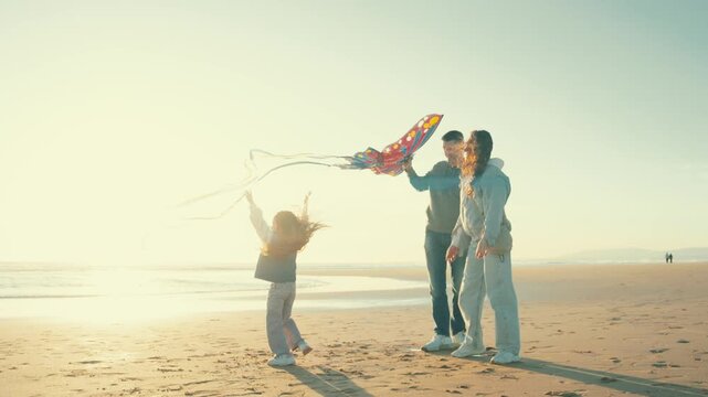 Family enjoys kite flying on the beach during sunset with child running and parents cheering