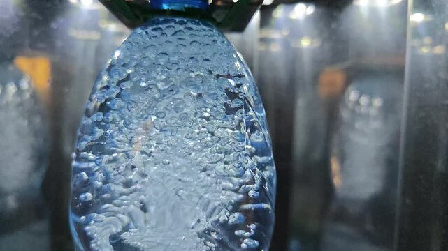 An industrial machine efficiently fills a plastic bottle with refreshing, bubbly carbonated water, creating a mesmerizing display of active bubbles and liquid movement during the high-speed beverage