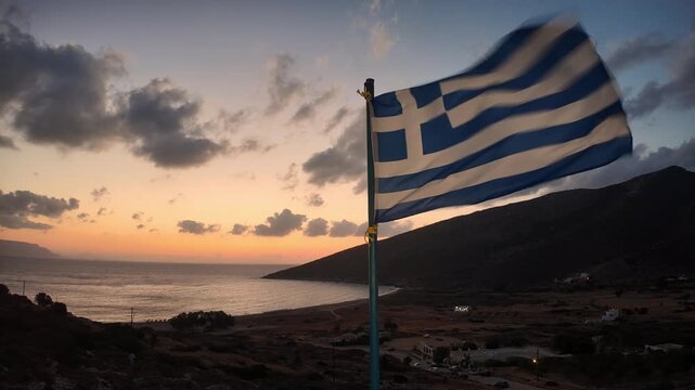 Beautiful view of a colourful sunrise at the Theodoti beach in Ios Greece, and the Greek flag waving in the air