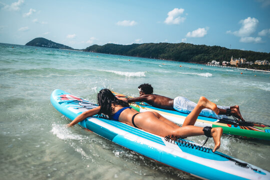 Young multiethnic people, couple having fun on surfboards in the clear ocean water during summer
