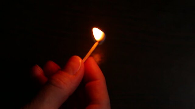 A woman strikes a match with her fingers against a matchbox. Burning match in her hand isolated on black background with empty copy space. Closeup