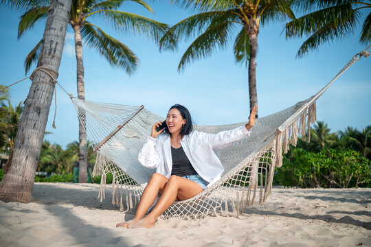 Cheerful woman talking on a smartphone during a sunny day at a tropical beach on summer vacation
