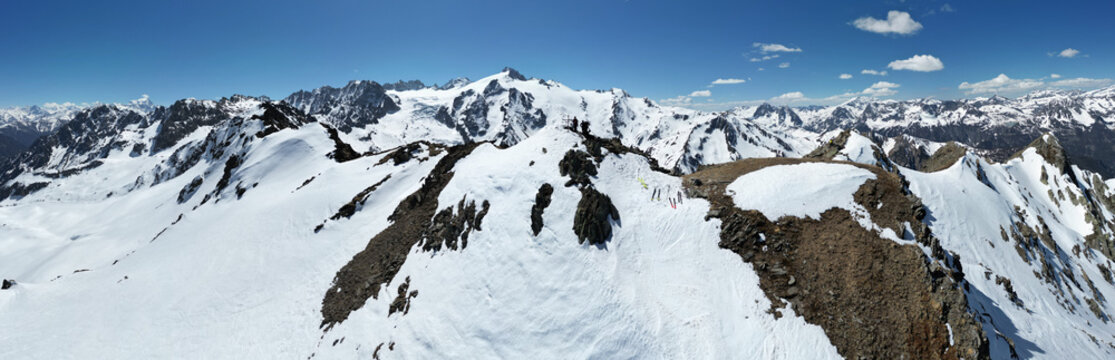 Aerial view of Pointe Ronde mountain peak with snow-covered ridges, rocky outcrops, and skiers standing on the summit under a clear blue sky in Trient, Valais, Switzerland.