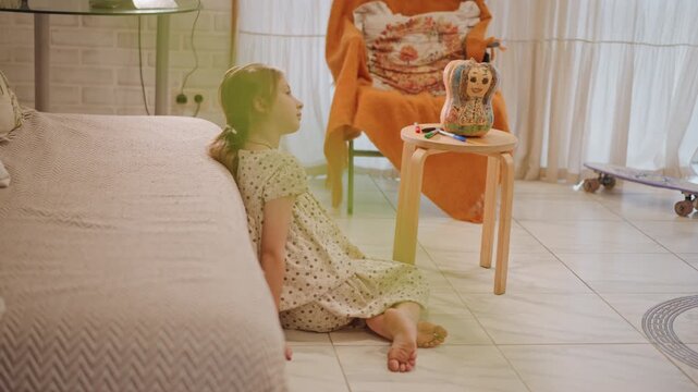 White girl gazing at pumpkin pie on stool, calm indoor afternoon with sunlight through curtains, leaning on sofa beside orange throw, tiled floor and patterned rug, doll beside pie, reflective
