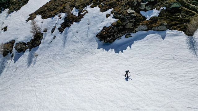 Aerial view of a lone skier traversing a snowy mountain slope near Pointe Ronde with rocky outcrops and scattered trees in Trient, Valais, Switzerland.