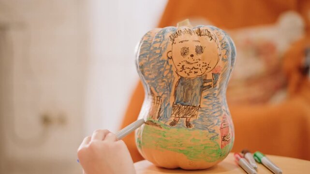 Closeup hands coloring painted pumpkin gourd with markers on wooden table, orange couch backdrop, illustrator adding color strokes, playful childlike doodles, cozy harvest atmosphere