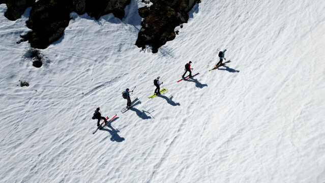 Aerial view of a group of ski tourers climbing a steep snowy slope near Pointe Ronde and rocky outcrops in Trient, Valais, Switzerland.
