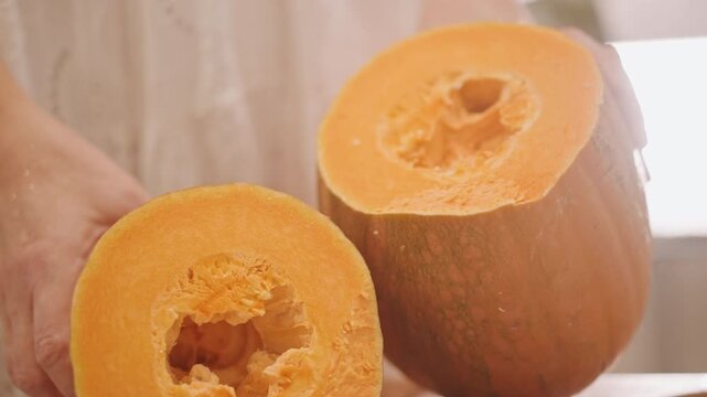 Halved pumpkin on wooden counter, hands of home baker holding hollowed halves, rich orange flesh and seeds removed, warm kitchen light, prepping puree for pumpkin pie, rustic cozy autumn baking scene
