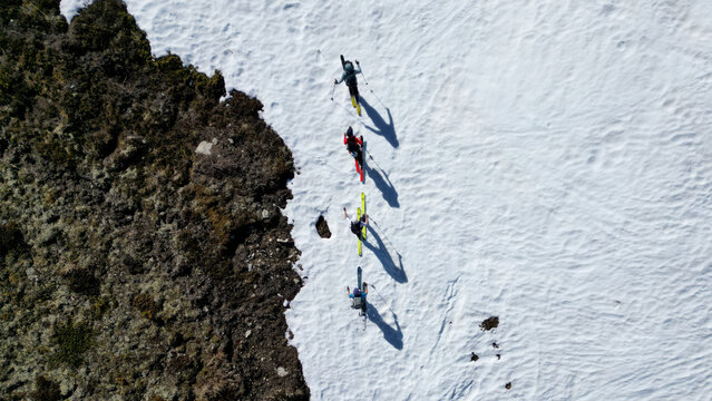 Aerial view of four ski tourers walking in a line on the snowy slopes of Pointe Ronde with long shadows and rocky terrain in Trient, Valais, Switzerland.