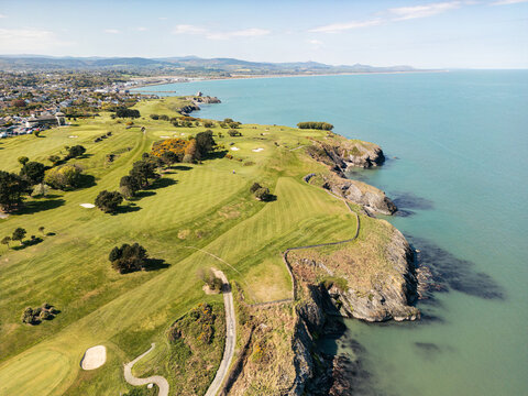 Aerial view of the lush green fairways and rugged cliffs of a coastal golf course overlooking the Irish Sea in Wicklow, County Wicklow, Ireland.