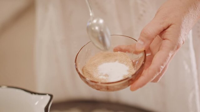 Hands mixing pumpkin spice mix in small glass bowl with spoon, sugar cinnamon and nutmeg combined, warm soft lighting, lace dress sleeve visible, closeup autumn baking preparation for pumpkin pie