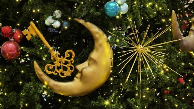 Gold key and anthropomorphic moon hanging on festive christmas tree with bright lights