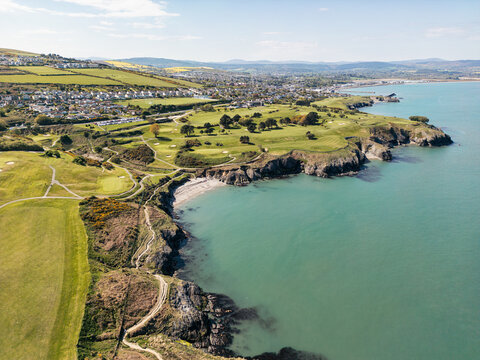 Aerial view of the rugged coastline featuring green golf courses and rocky cliffs overlooking the turquoise sea in Wicklow, County Wicklow, Ireland.