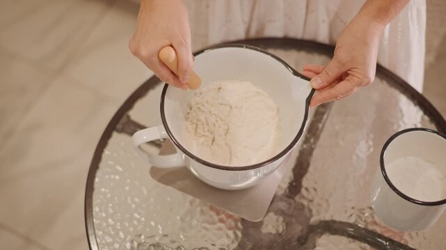 Overhead caucasian hands whisking flour over glass table, precise circular motions, enamel bowl placed on reflective surface, quiet pastry prep, focused chef technique and careful portioning
