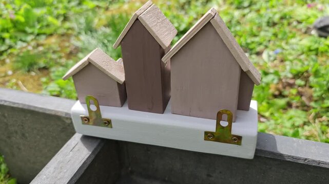 Captivating detailed shot of a handcrafted wooden key holder resembling a small village of miniature houses, adorned with subtle decorative elements, positioned outdoors with a lush, sunlit green