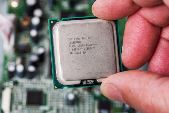 precision electronic component of a processor Intel Celeron with contacts in a hand, against a printed circuit board.