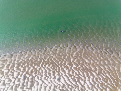 Aerial view of intricate sandbar patterns and a small boat in the green river water Gaibandha, Rangpur Division, Bangladesh.