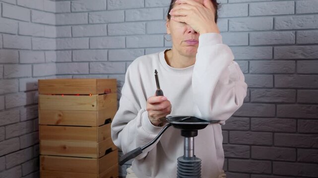 Frustrated woman failing to assemble an office chair. Stressed and confused adult woman experiencing difficulty and failure while trying to assemble a broken office chair with a screwdriver