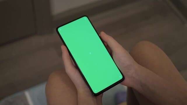 Young Woman Use Phone in Toilet. Green Screen Mobile Phone for Copy Space Indoors of Toilet or Bathroom. Chroma Key Mock-up on Smartphone in Hand. Girl Using Phone With Green Screen in Bathroom.