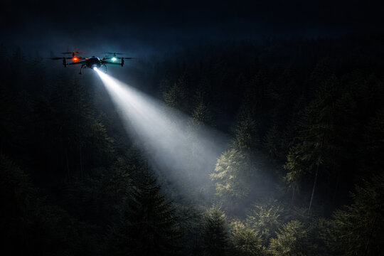 Drone illuminating forest with powerful searchlight in dark night