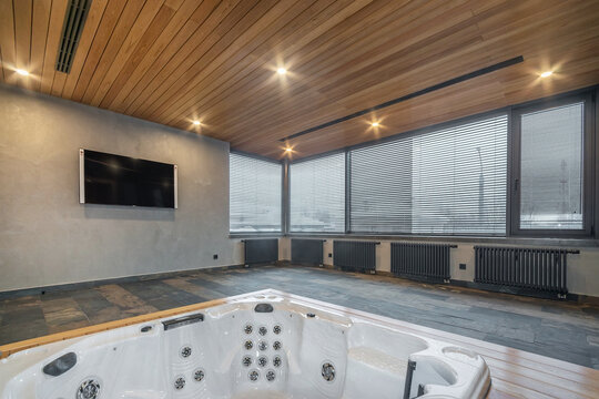 A modern hot tub in a spacious room with panoramic windows, wooden ceiling and stone floor.