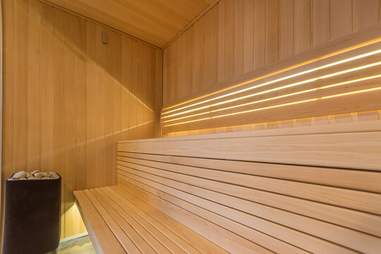 A new sauna made of light wood with benches, a heating element and soft lighting.
