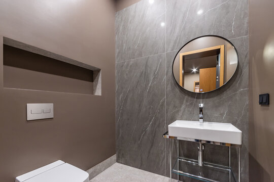 Minimalistic bathroom design decorated with brown marble tiles. Accessory shelf, modern design of the sink stand.