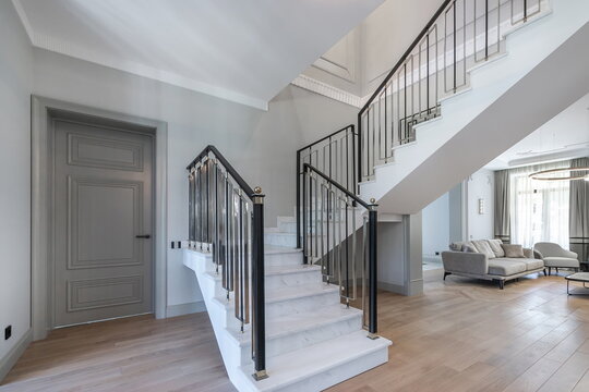 The hall of a country house in neoclassical style with an open plan and a staircase with elegant railings.