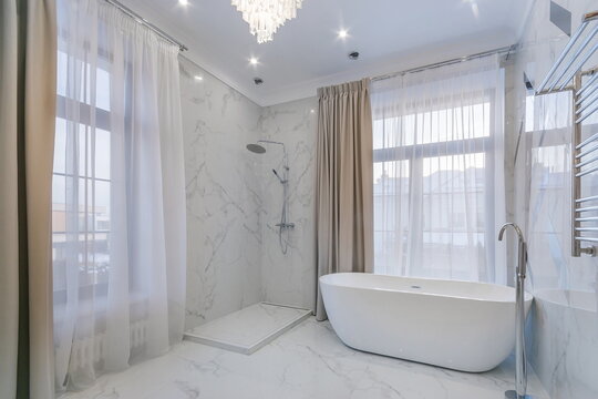 The bathroom is decorated with white marble tiles, with a bathtub by the panoramic window.