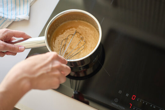 Hands whisking brown sauce in small saucepan on induction cooktop