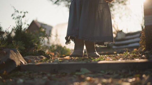 Boots on garden steps at dusk, slow purposeful stride with bundle of herbs, warm backlight and scattered leaves, vintage skirt hem and textured soles create earthy domestic mood of harvest returning