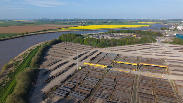 Aerial view of PD Ports industrial facility with stacks of steel beams and yellow gantry cranes by the river in Scunthorpe, England, United Kingdom.