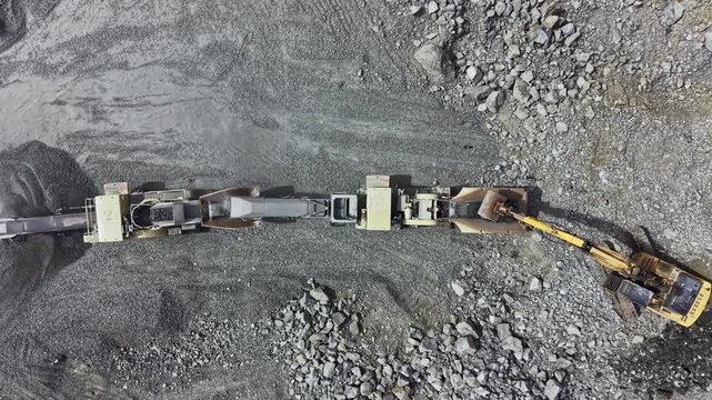 Heavy machinery is at work in a granite quarry for stone extraction in a rugged area with gravel and rocks.