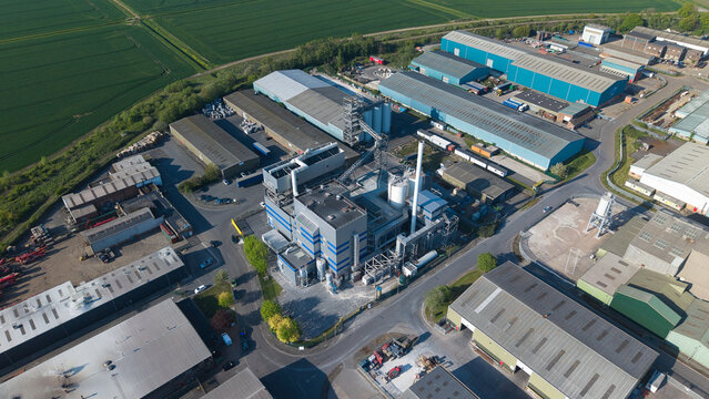 Aerial view of Flixborough Industrial Estate featuring large warehouses, factory structures, and silos surrounded by green fields under a clear sky in Flixborough, England, United Kingdom.