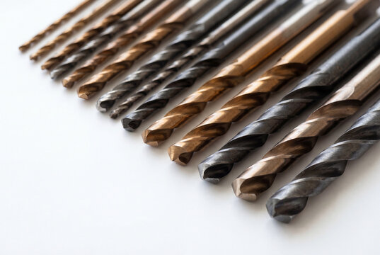 Set of metal drill bits arranged by size on white surface