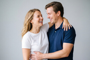 Fototapeta premium Happy young couple hugging and laughing together while standing on grey background