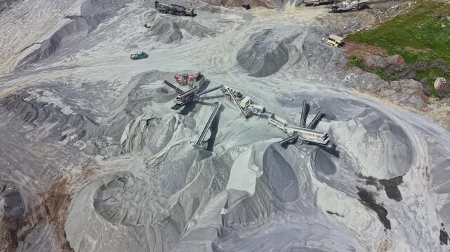 Heavy machinery operates in a granite quarry moving large amounts of stone and soil on a sunny day with stockpiles visible