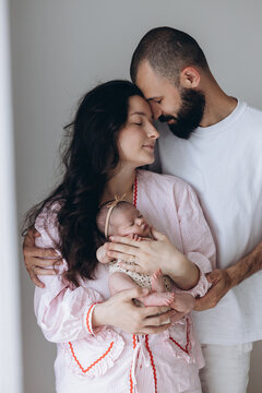 New parents gently cradle their sleeping baby in soft, natural light
