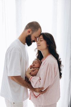 Young couple tenderly holding newborn baby in softly lit home setting