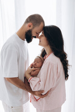 Young couple tenderly holds newborn baby in soft natural light indoors