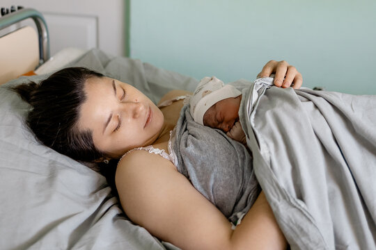 New mother rests peacefully holding her newborn baby wrapped in soft blanket in hospital room