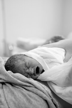 Newborn baby cries softly wrapped in cloth resting on mother&rsquo;s chest in hospital room