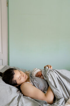 Newborn baby sleeps peacefully wrapped in gray blanket held close by mother resting in bed