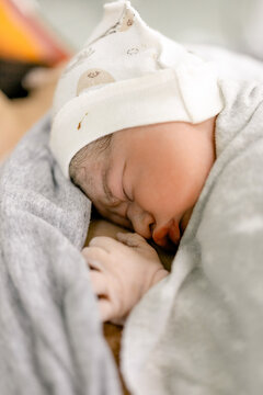 Newborn baby sleeps peacefully wrapped in soft blanket wearing tiny hat