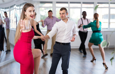 Fototapeta premium Positive woman and man dancing foxtrot in pair during group dance party