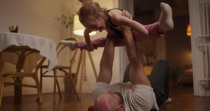 Joyful laughter fills the air as a little girl and her dad create fun memories while playing acrobatics at home